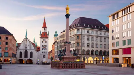 Mariensäule mit einer golden Statue an der Spitze auf dem Marienplatz. Der Platz ist umgeben von Häusern.