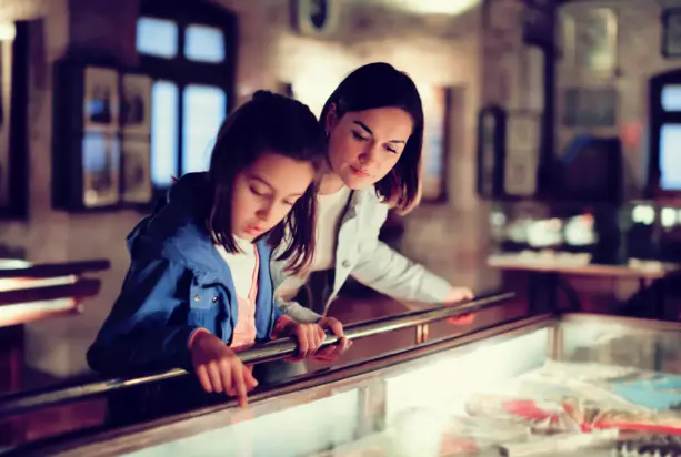 Eine Frau und ein Mädchen stehen vor einer Vitrine in einem Museum und schauen sich etwas an.