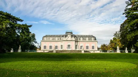 Schlossgarten mit Bäumen und das Schloss Benrath am Tag.