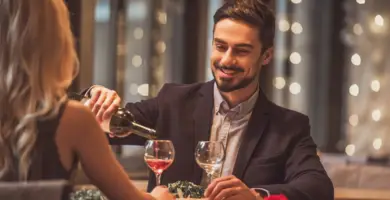 Ein Paar sitzt am Tisch. Der Mann gießt einen Rotwein ein.