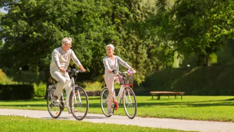 Älteres Paar fährt freudig auf Fahrrädern durch den Park.