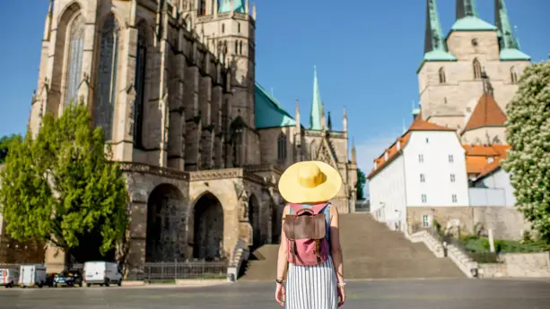 Eine Frau mit einem großen gelben Hut steht auf dem Domplatz und schaut zum Erfurter Dom.