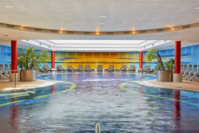 Piscine avec un grand bassin et des chaises longues au bord.