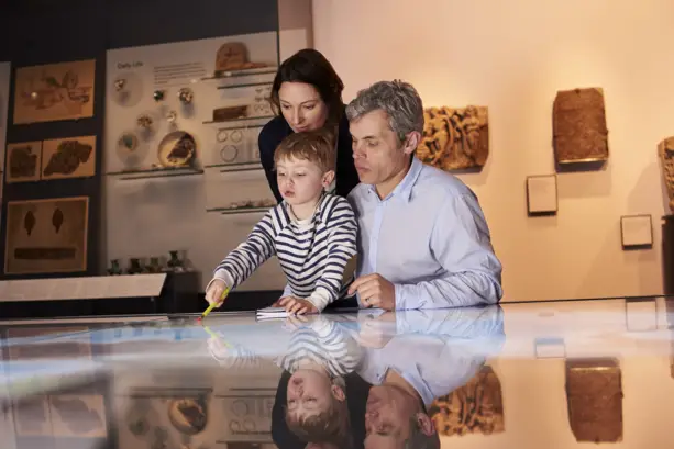 Eltern schauen mit ihrem Sohn in eine Vitrine im Museum. Der Junge zeigt mit einem Stift auf etwas.