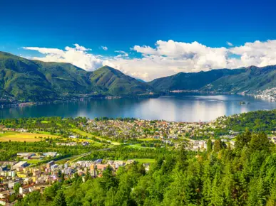 Blick auf Locarno und dem Lago Maggiore am Tag. Im Hintergrund sind eine Bergkette.