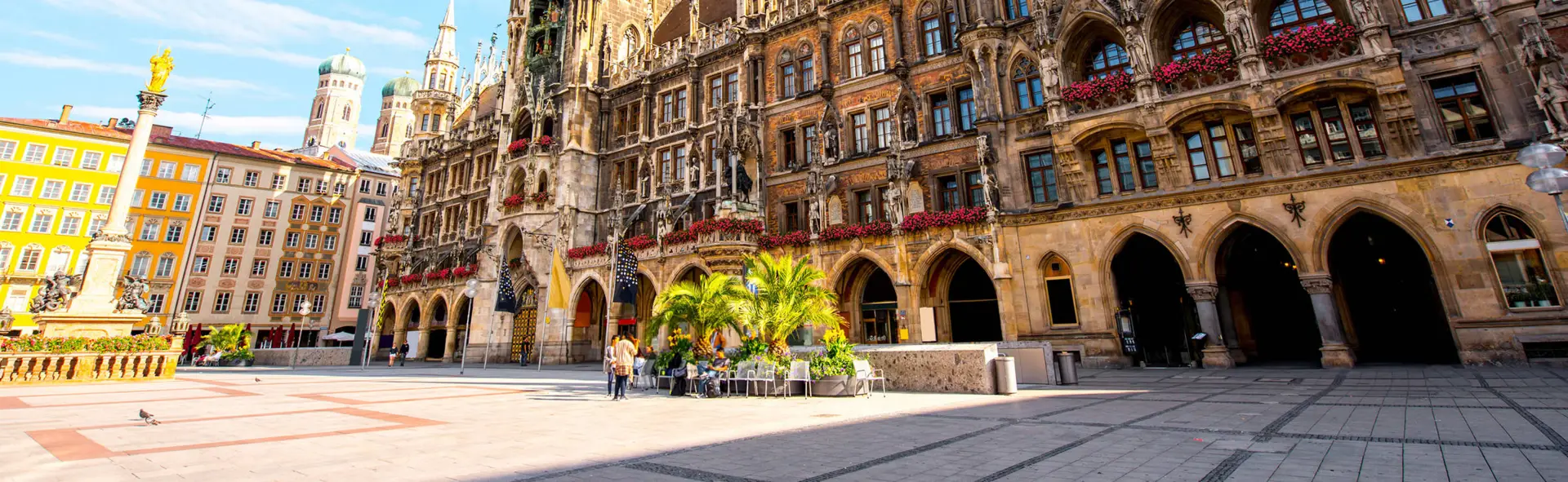 Marienplatz mit Sitzmöglichkeiten vor dem Neuen Rathaus. Das Rathaus wird von der Sonne angestrahlt.