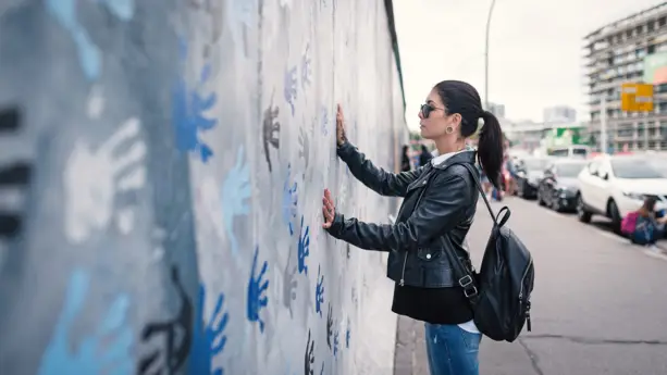 Eine Frau in einer schwarzen Lederjacke und Tunnel im Ohr berührt einen Teil der Mauer in der East Side Gallery.