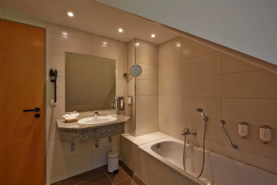 Salle de bain avec un lavabo et une baignoire à côté. Un miroir est suspendu au-dessus du lavabo.