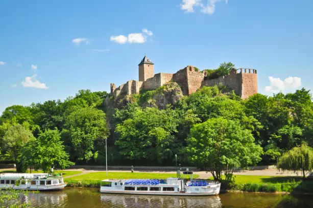 Blick auf die Burg Giebichenstein  von der Saale aus. Im Vordergrund stehen zwei Fähren.