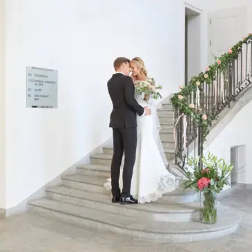 Ein Hochzeitspaar steht innig auf einer geschmückten Treppe im Palais Besenvahl.