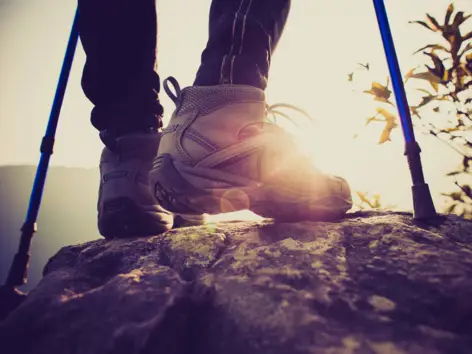 Nahaufnahme auf die Wanderschuhe und Wanderstöcke eines Wanderers.