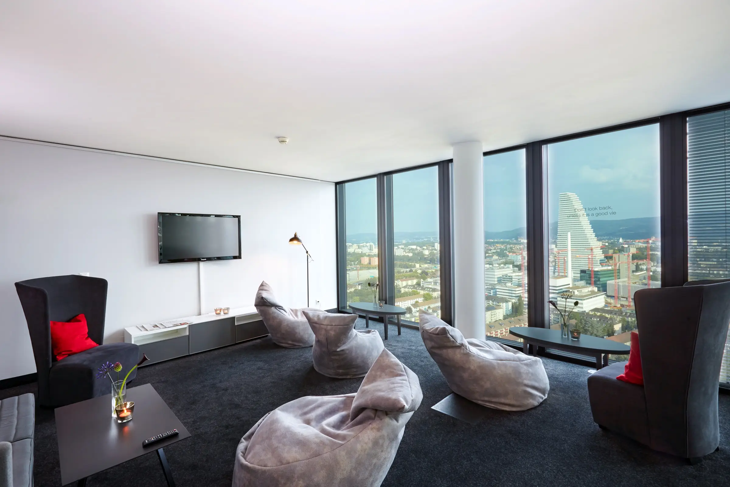 Vereinzelte Sitzecken mit weichen Sitzen und 2 Ohrenstühlen. Auf der rechten Seite sind bodentiefe Fenster mit dem Blick auf die Stadt.