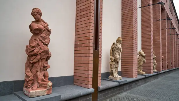 Verschiedene weibliche, römische Statuen in rot und beige an der Hauswand.