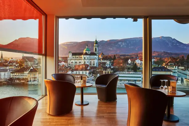 Hotelbar mit großen Fenstern und Blick auf die Aare und auf Solothurn. Vor dem Fenster stehen ein paar Sessel.