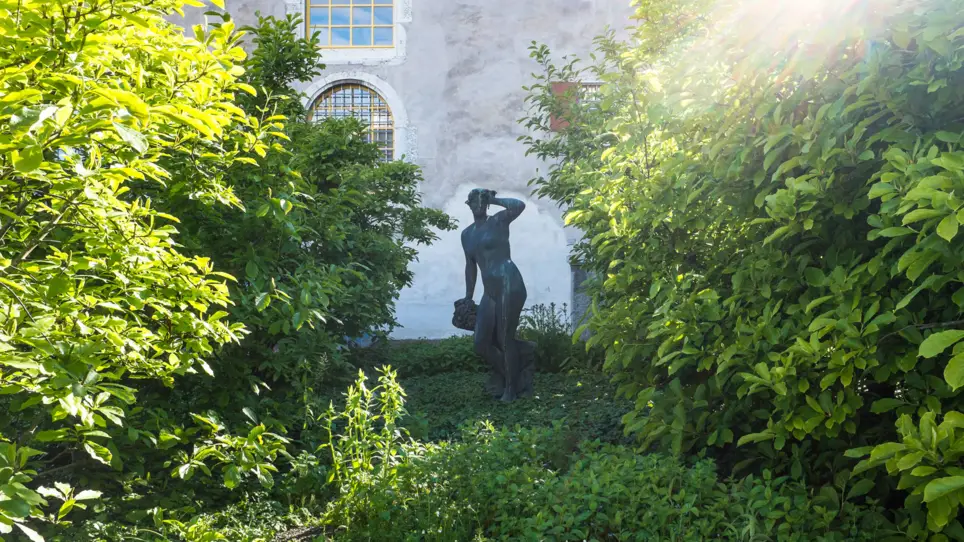 Eine Frauenstatue steht zwischen Büschen im Garten vom Palais Besenvahl.