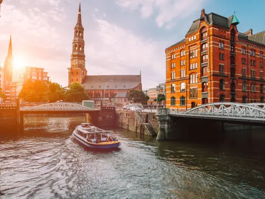 Speicherstadt mit Backsteinhäusern an der Elbe. Auf dem Fluss fährt eine Fähre.