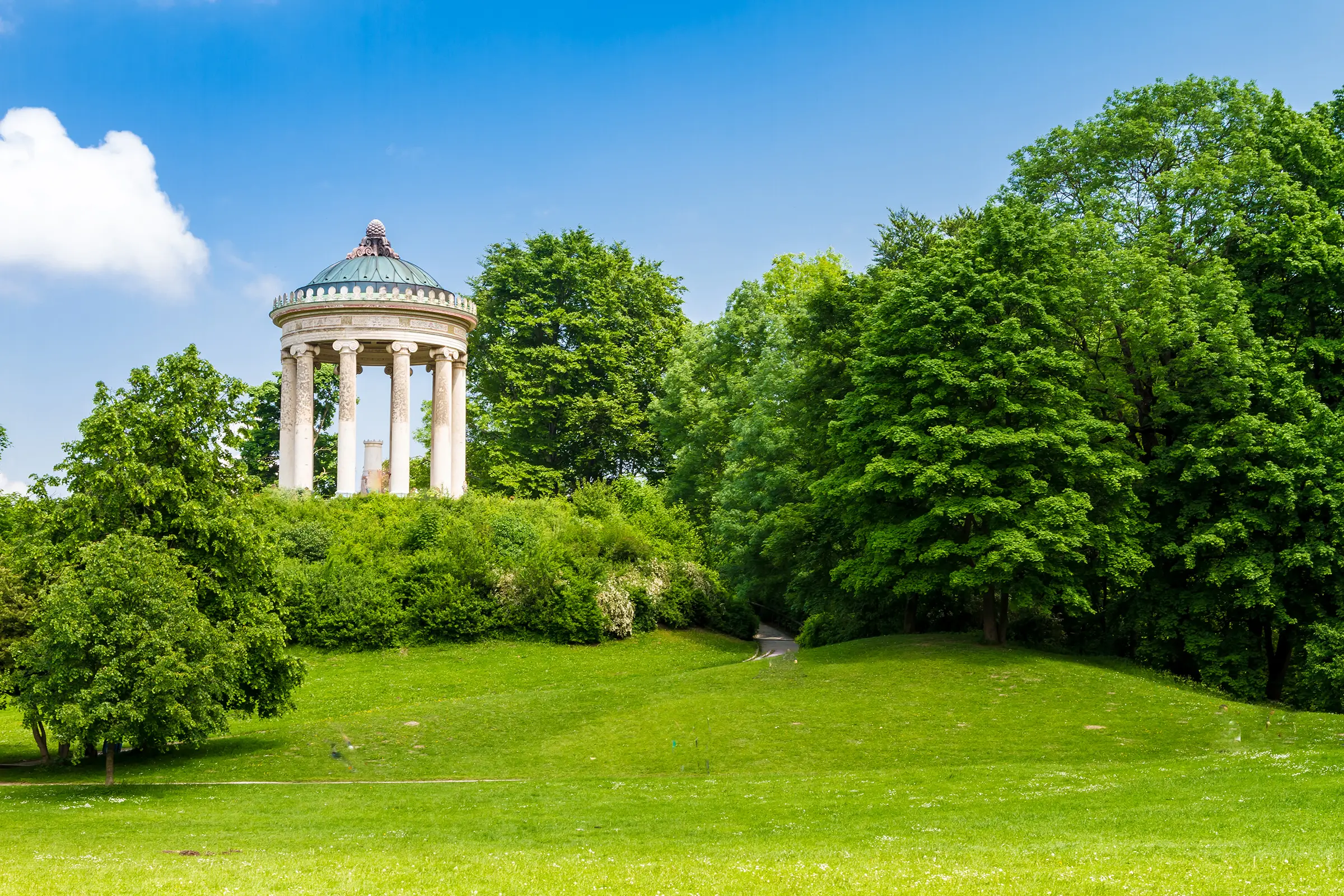 Garten mit Büschen und Rasen. Im Hintergrund steht ein griechisch aussehender Pavilion