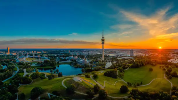 Blick über den Olympiapark und München, während die Sonne untergeht. In der Mitte steht der Olympiapark.