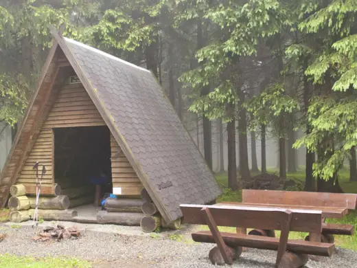 Eine kleine Holzhütte mit Sitzbänken davor im Wald.