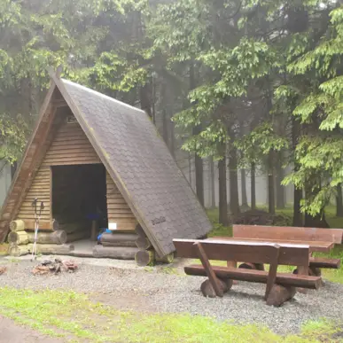 Eine kleine Holzhütte mit Sitzbänken davor im Wald.