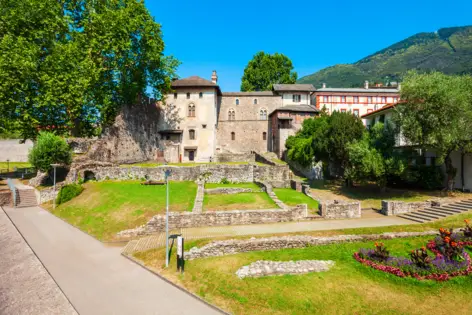 Castello Visconteo mit Mauerresten und einer Wiese. Im Hintergrund stehen Berge.