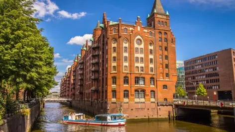 Backsteinhaus in der Speicherstadt. Auf dem Wasser fährt ein Boot entlang.