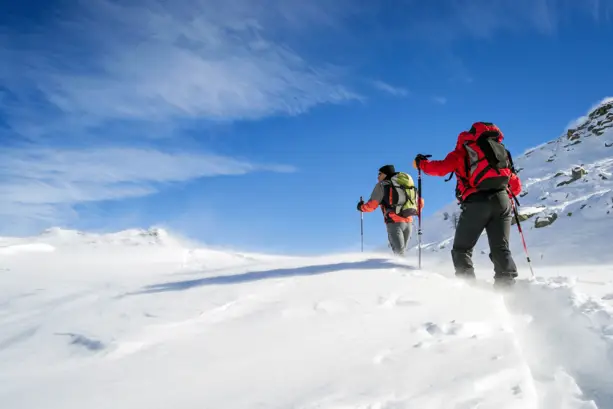 Zwei Schneeschuhwanderer auf einer Bergspitze mit tiefem Schnee.