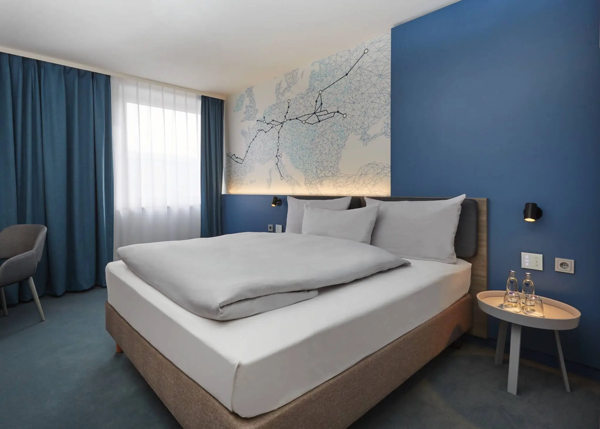 Modern gestaltetes Hotelzimmer mit einer blauen Wand. An der Wand hängt eine in linien gestaltete Europakarte mit dicken Linien abgehend von Leipzig.