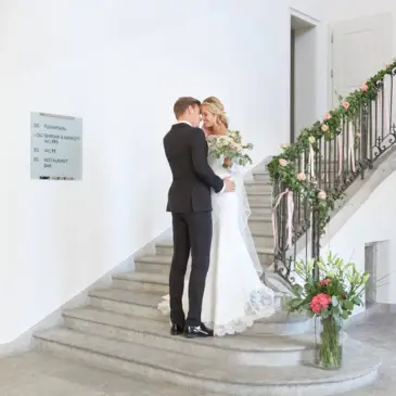 Ein Hochzeitspaar steht innig auf einer geschmückten Treppe im Palais Besenvahl.