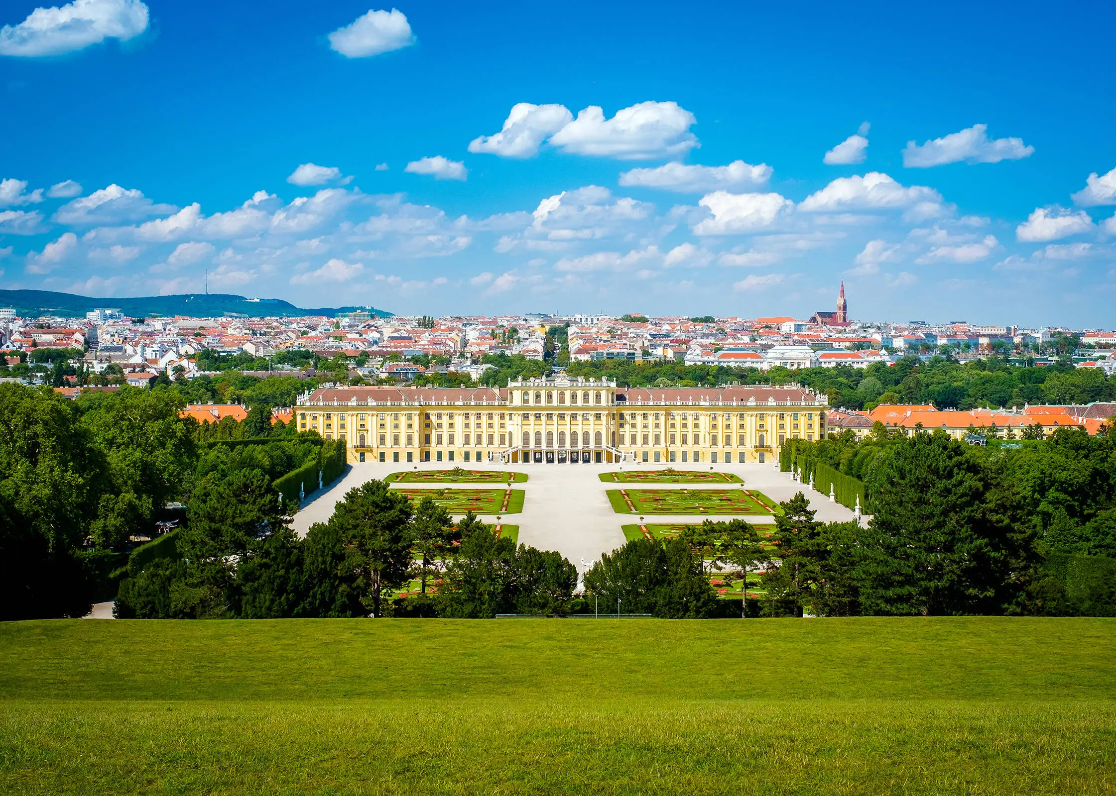 Blick auf das Schloss Schönbrunn mit dem dazugehörigen Schlosspark. Im Hintergrund ist die Stadt Wien.