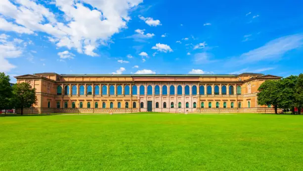 Alte Pinakothek mit roten und braunen Fassade. Davor ist eine große Liege.