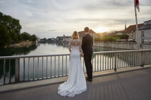 Ein Hochzeitspaar steht auf einer Brücke und schaut auf die Aare, während die Sonne untergeht.