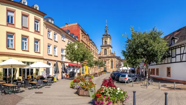 Straße mit Cafés zum St. Johann. An der Straße stehen große Blumenkästen.