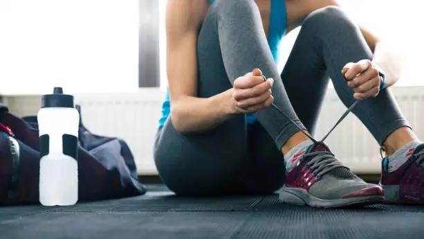 Eine Frau in Sportkleidung sitzt auf dem Boden und schnürrt sich die Schuhe zu.