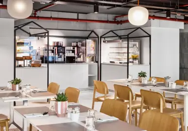 Tables and chairs in the restaurant with coffee machine and storage space for breakfast buffet in the background.