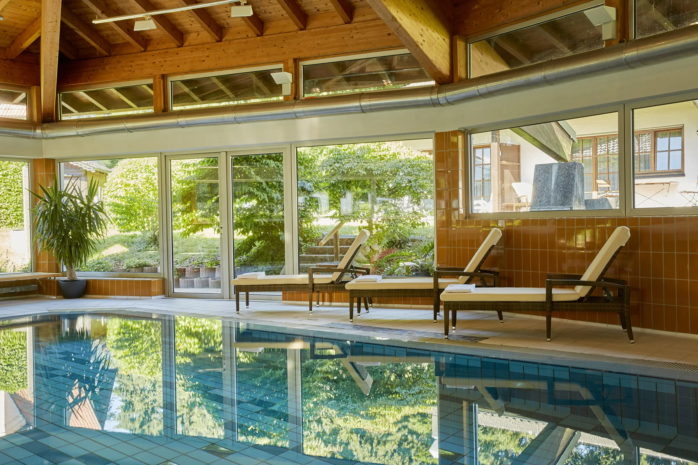 Pool mit Rundumverglasung und Blick in den Garten vom Hotel. Am Rand stehen Liegen.