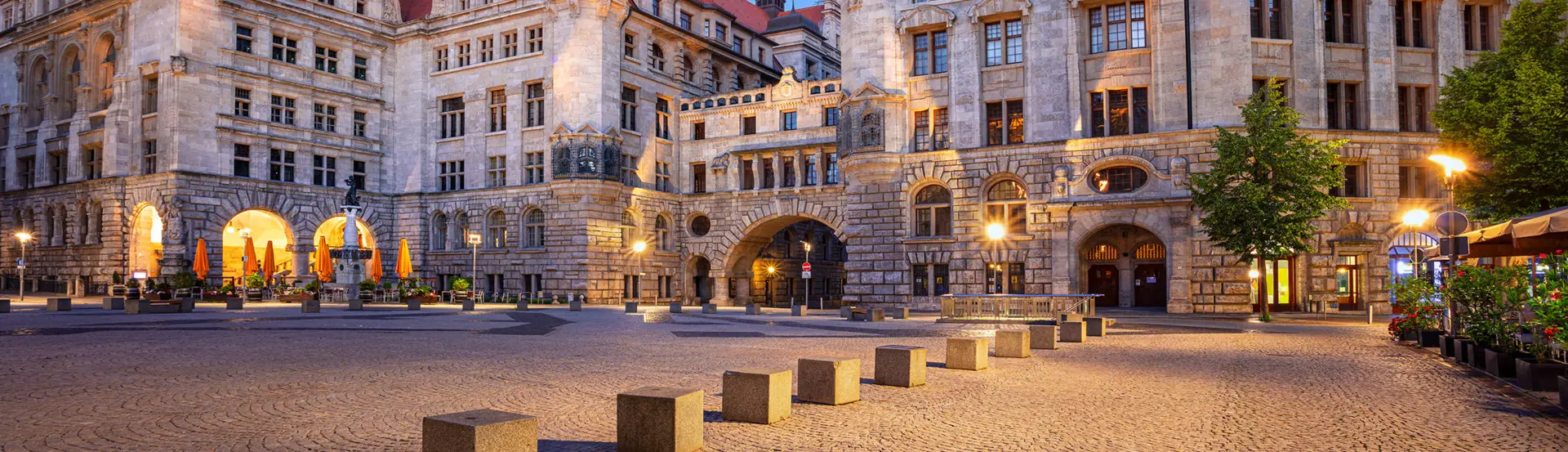 Beleuchteter Burgplatz vor dem Neuen Rathaus in Leipzig bei Nacht. Um den Platz sind viele Restaurants.