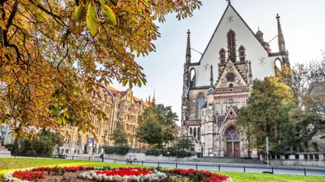 Thomaskirche im Herbst mit einem großen, runden Blumenbeet davor.