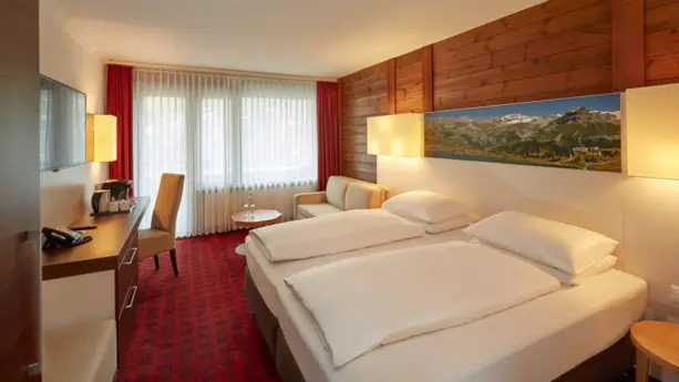 Großes Doppelbett und ein Schreibtisch im Hotelzimmer. Eine Wand ist mit Holz vertafelt.