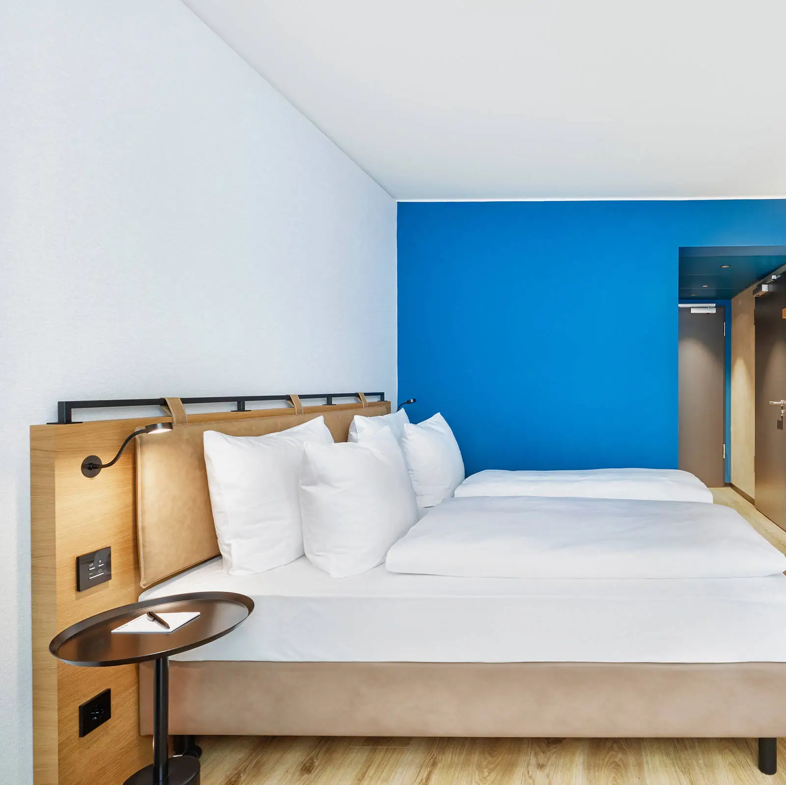 Hotelzimmer mit einem Doppelbett in dunkelbraunen und blauen Farben. Vor dem Bett hängt ein Fernseher.