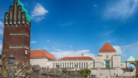 Hochzeitsturm auf der linken Seite und ein Ausstellungsgebäude in der Mitte. Auf dem Gebäude balanciert eine Statue.