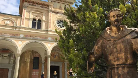 Eingang von der Madonna del Sasso mit einer goldenen Mönchstatue und einem Baum im Vordergrund