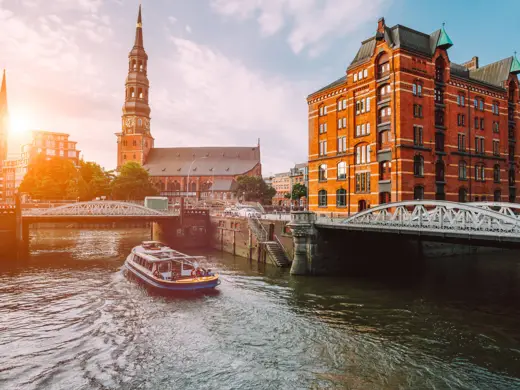 Hamburger Speicherstadt bei Tag mit einem Schiff auf dem Kanal. Im Hintergrund steht der Michel.