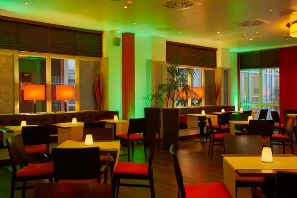 Grün beleuchtete Hotelbar mit zahlreichen Tischen.