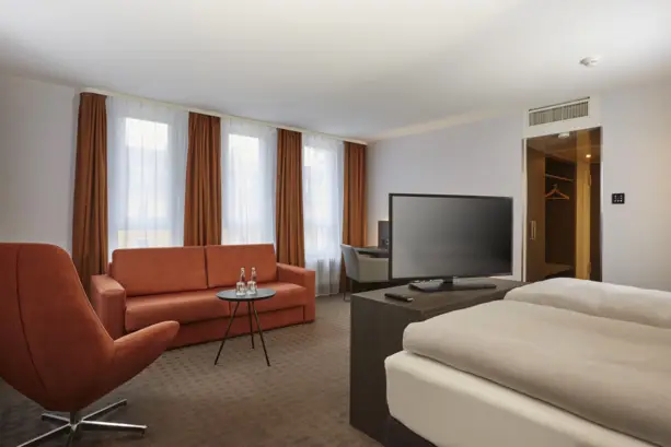 Hotelzimmer mit roter Couch und rotem Stuhl. Hinter der Couch sind 3 große Fenster.