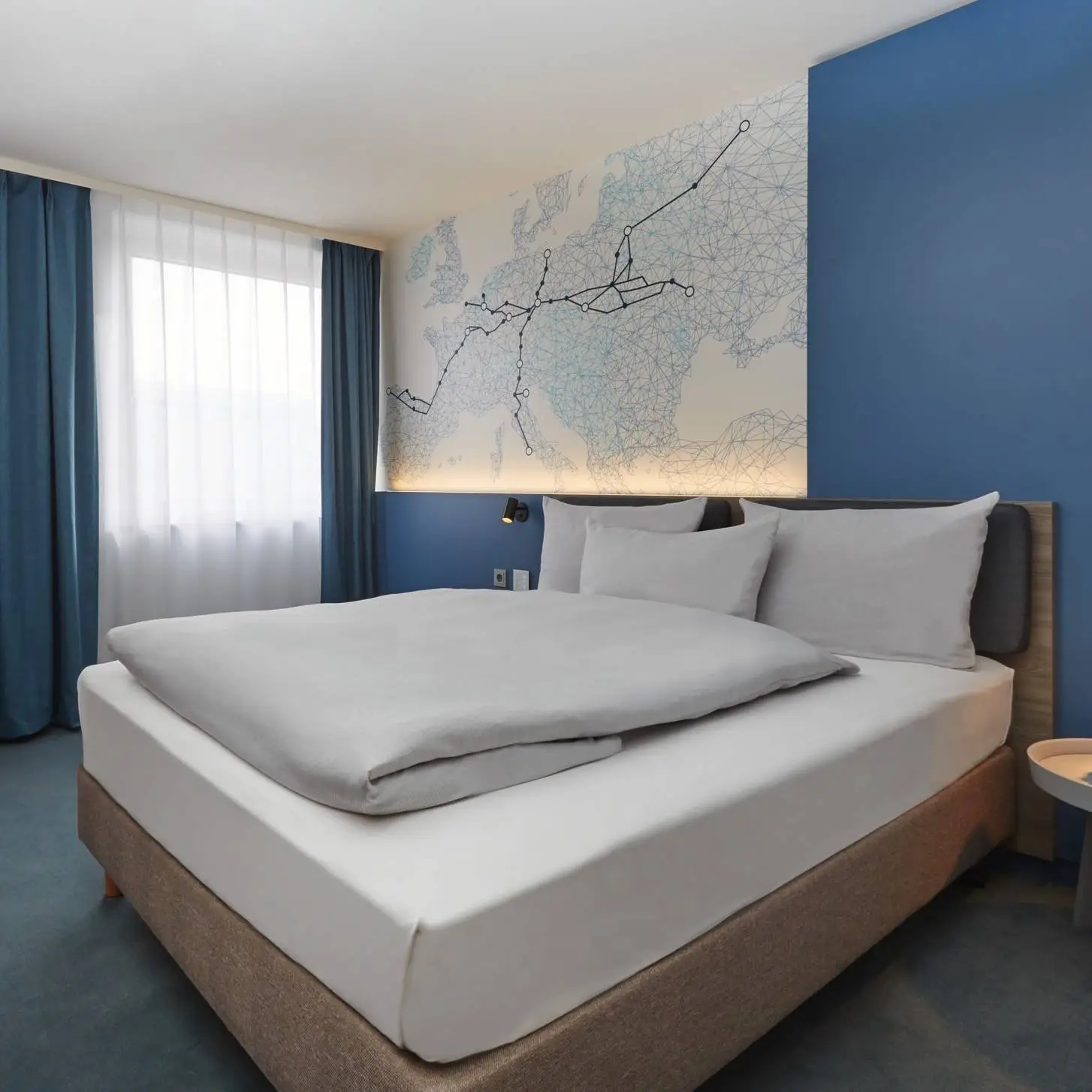 Modern gestaltetes Hotelzimmer mit einer blauen Wand. An der Wand hängt eine in linien gestaltete Europakarte mit dicken Linien abgehend von Leipzig.