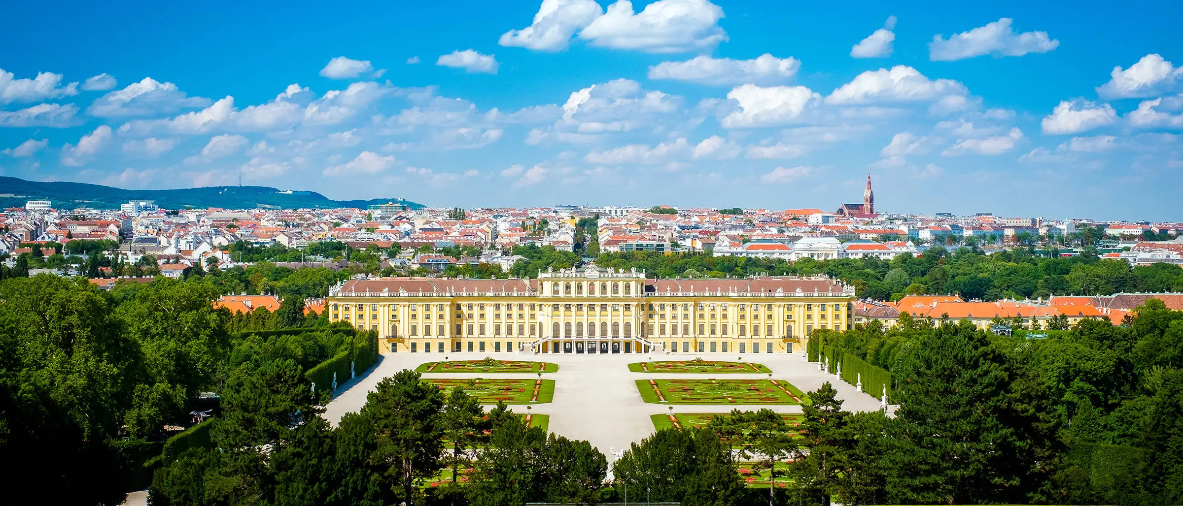 Blick auf das Schloss Schönbrunn mit dem dazugehörigen Schlosspark. Im Hintergrund ist die Stadt Wien.