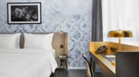 Doppelbett mit einem goldschwarzem Schreibtisch daneben. Das Bett steht vor einer blauen Wand.