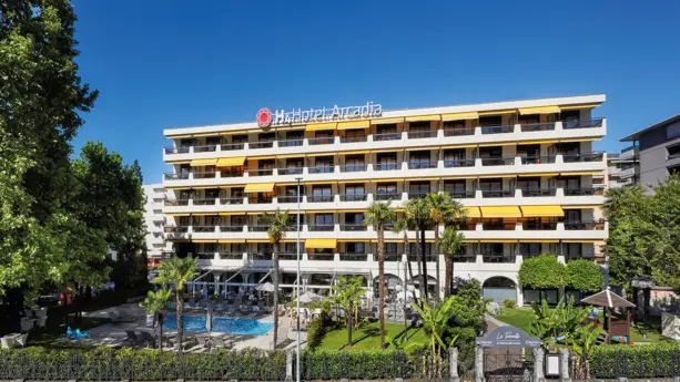 Außenansicht vom Hotel mit Balkonen. Vor dem Hotel stehen Palmen und ein Pool.