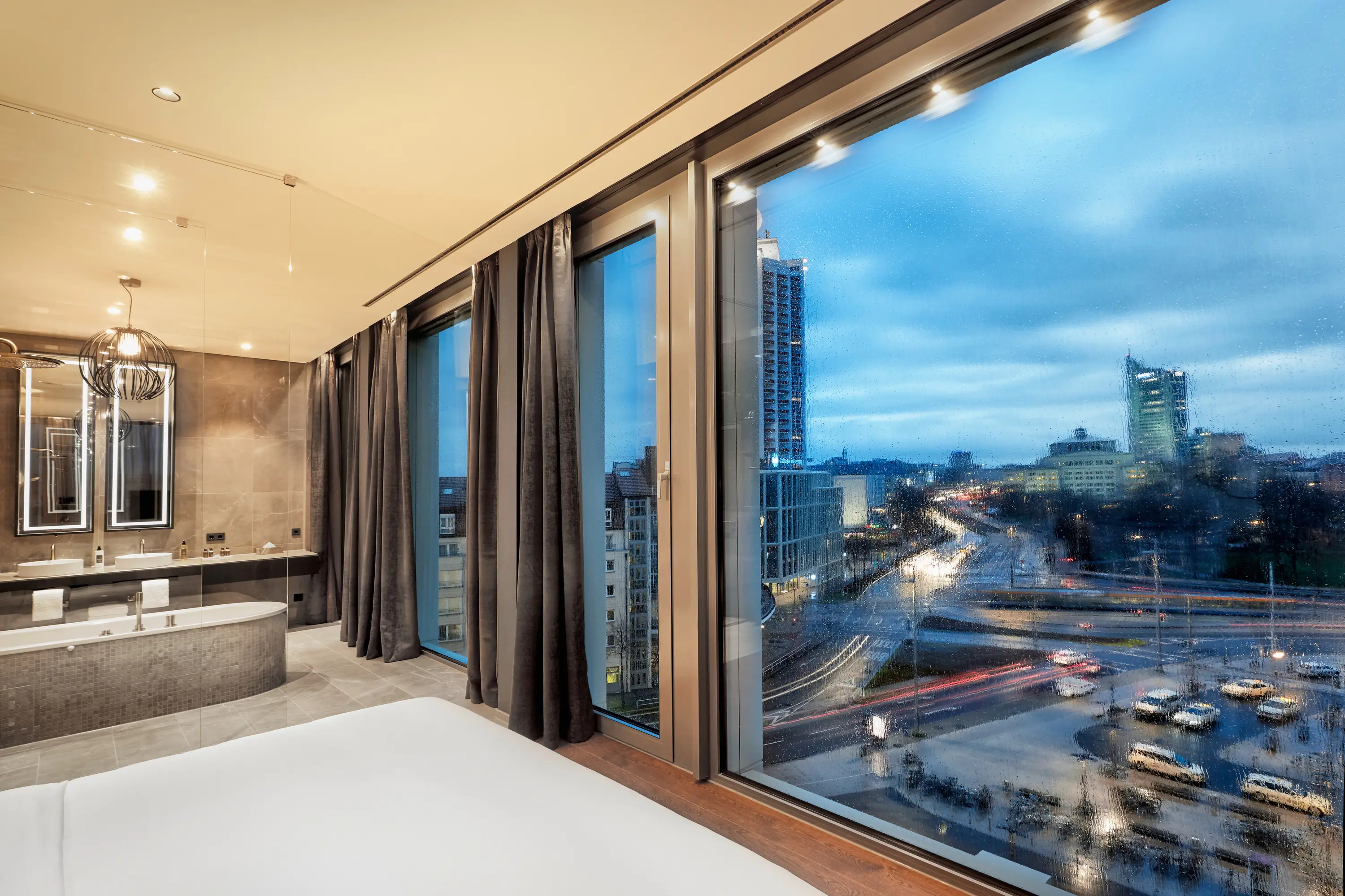 Bodentiefe Fenster mit Blick auf die Stadt. Auf der linken Seite steht eine freistehende Wann und ein Waschbecken.